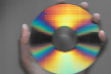 Hand holding compact disc against blue