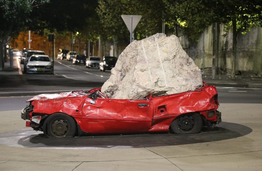 Boulder crushing damaged red car