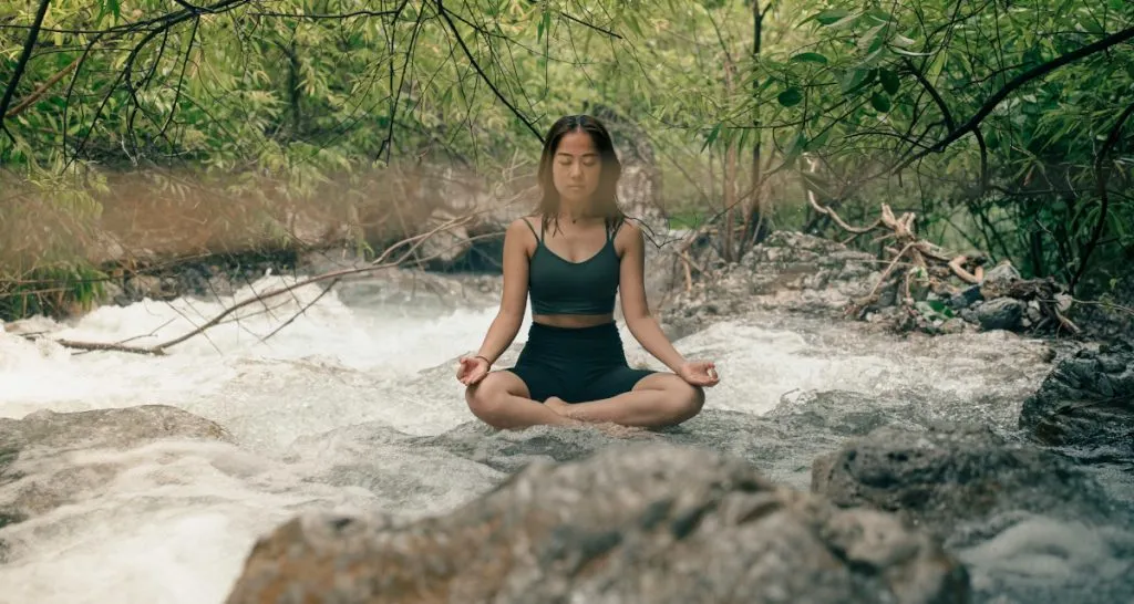 Person meditating near flowing river